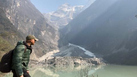 BBC World Service environment correspondent Navin Singh Khadka trekking with mountains visible behind him
