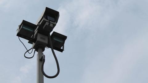 A tall CCTV camera against a blue cloudy sky 