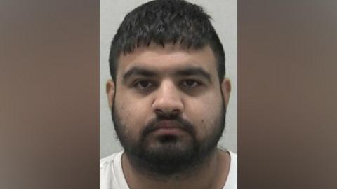 Mugshot of Hasan Mohammed. He has thick black hair and a thick black beard.