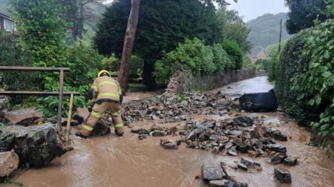 A firefighter clearing a flooded road with rocks strewn along it