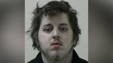 Mugshot of Dorritt. He has long scruffy brown hair, a faint moustache and wispy fair hair on his chin. 