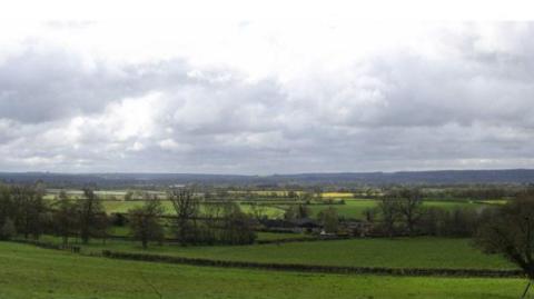 Rolling green fields with rows of hedges, trees and hills in the far distance