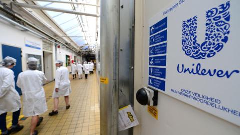 Unilever staff in white coats and caps at its Rotterdam headquarters with a Unilever sign on the right