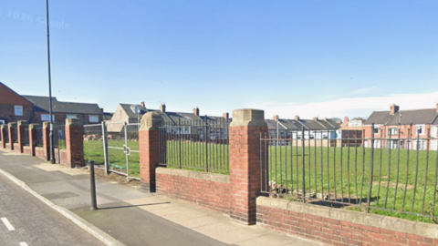 An open stretch of grassy land off Seaside Lane in Easington. The school was demolished several years ago. The site is surrounded by a brick wall and metal fence perimeter.