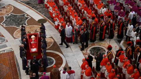 Pallbearers carry the Pope's coffin into position as clerics watch on.