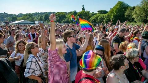 A crowd of several hundred people raise their hands in the air and wave rainbow flags during a Pride event in Durham.