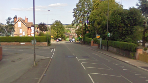 The junction of a side road and more main road through a residential area. There is a yellow speed camera visible.