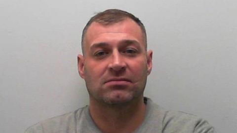 A man in a grey prison tracksuit against a grey background
