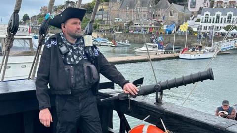 A police officer stood on a ship, wearing a pirate hat, looking into the distance.