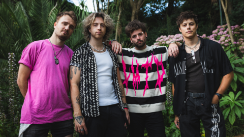 (Left to right) Josh Rose, Sparxx Jenkins, Ash Jenkins and JV stand in an ornamental gardens in a publicity photo. Ash is resting his arms on the shoulders of the bandmates beside him.