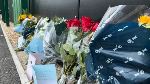 A number of floral and card tributes left for the late Billy Vigar at Chichester City football club. Six separate floral tributes can be seen in a row alongside three cards. 