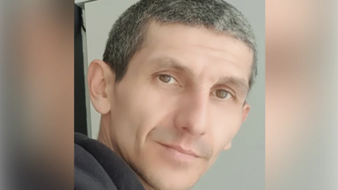 Man with short grey hair - he has brown eyes and is looking at the camera with his head turned to the right - he has a slight smile.