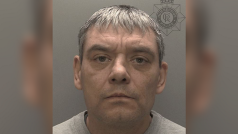 A police head and shoulders shot of a man - Kurt Taylor - looking at the camera. He has short grey hair and is wearing a grey sweater. The wall behind him is grey.