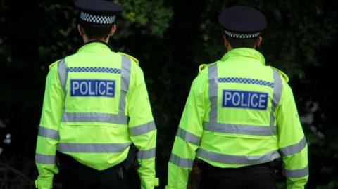 Two police officers walking away from the camera. They are wearing hi-vis jackets with POLICE written on the back.
