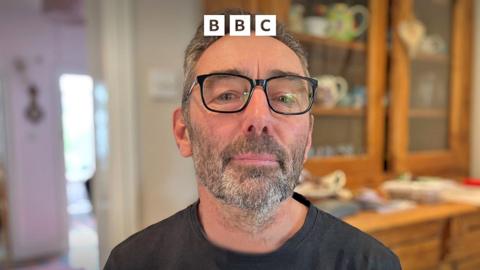 A man wearing glasses and a black t-shirt.
