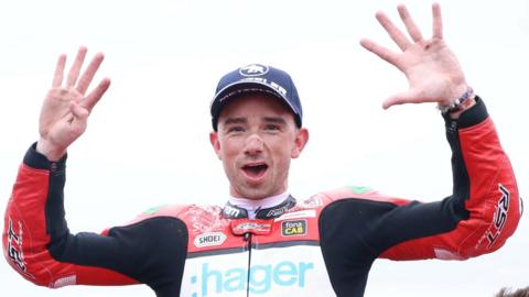 Glenn Irwin in a celebratory pose with his hands raised and a smile on his face