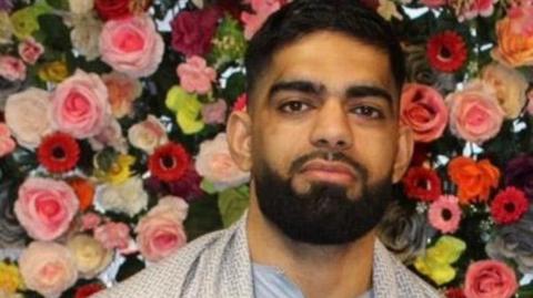 Luqman Ishfaq stands in front of a backdrop of pink and red flowers.