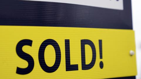 An estate agent's board, with the word 'sold!' in blue capital letters on a yellow background.