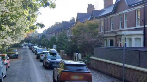 Google streetview of terraced houses lining the right of the street with cars parked in front. Trees and other cars line the left side of the road.