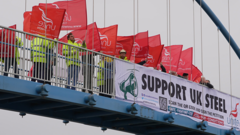 Unite members on bridge waving flags behind sign which reads "support UK steel"