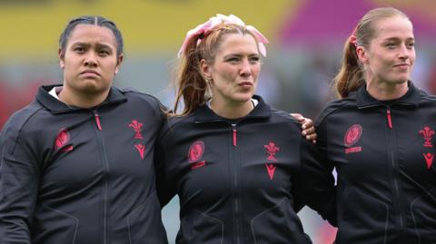 Sisilia Tuipulotu, Georgia Evans and Lisa Neumann stand arm in arm for the national anthem
