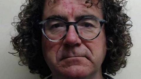 A mugshot of Roderick Bryce-Hagain, who has shoulder-length dark hair.