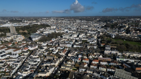 Ariel shot of South St Helier. Jersey. There are rows of houses and buildings below. The photo was taken on a cloudy day.