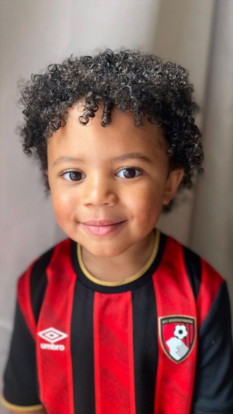 Arlo smiles at the camera. He has curly black hair and wears a red and white striped AFC Bournemout jersey.