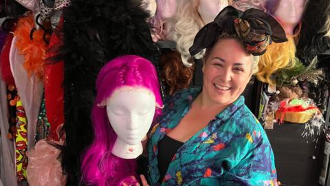 Kirsty Minchella-Storer dressed in a blue shirt holding the head of a manakin with a pink wig on 