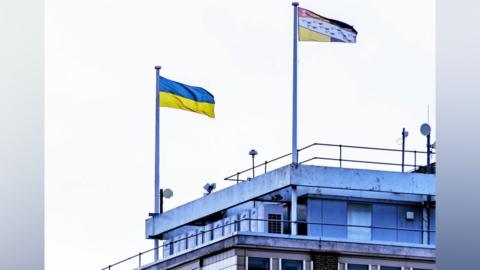 A Ukrainian flag and Norfolk county flag fly from flagpoles attached to Norfolk County Hall in Norwich