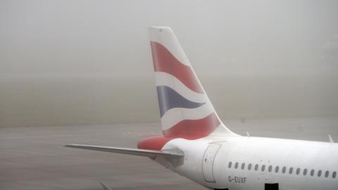 rear end of a British Airways plane in the fog at airport terminal, union flag pattern on tail