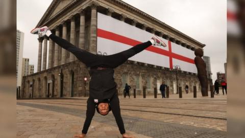 Joe Fraser doing a handstand in front of the flag