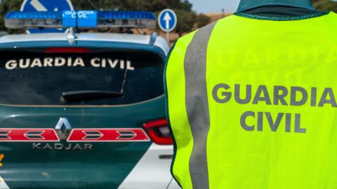 Civil guard agent wearing his reflective vest, next to the patrol car on a road.