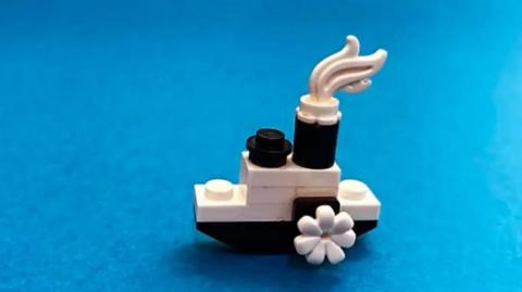 A small lego steam boat using black and white bricks is on a blue background