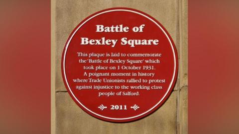 A red plaque on a brown stone background, reads in white writing: Battle of Bexley Square. This plaque is laid to commemorate the ' Battle of Bexley Square' which took place on 1 October 1931. 