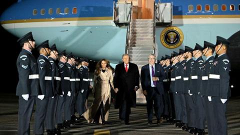US President Donald Trump and US First Lady Melania Trump disembark from Air Force One with a line of army personnel on each side 