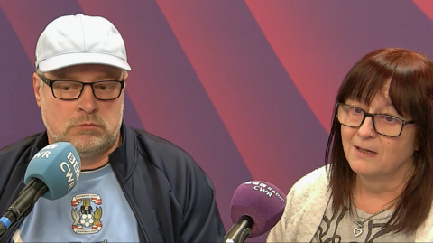 A man and a woman sat in a radio studio talking into microphones