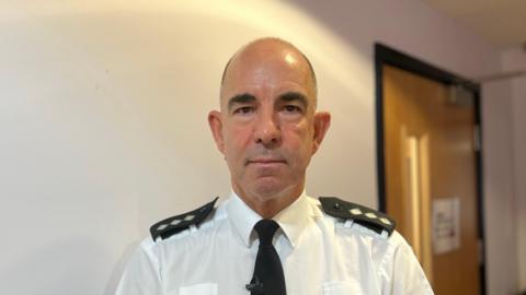 Insp Chris Beechey is standing in front of a white wall. He's wearing his police uniform and looking into the camera.