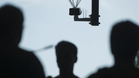 Passersby walk under a surveillance camera which is part of facial recognition technology test