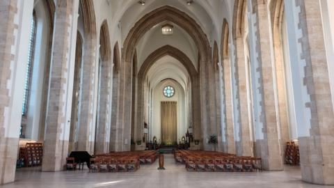 The inside of Guildford Cathedral. There are very high ceilings and two rows of chairs flanked either side of an aisle leading to the altar.