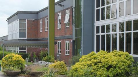 Chiltern Hills Academy, showing a school with red brick, a large number of windows, and a number of bushes and plants. 