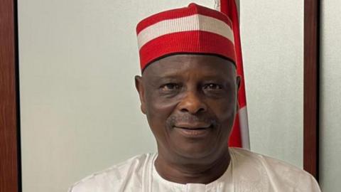 Rabiu Kwankwaso looks ahead, wearing his trademark red cap and a white top.