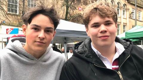 University students Joe Crowe, left, and Sam Whitworth in the city centre. Both are stood in front of a market stall.