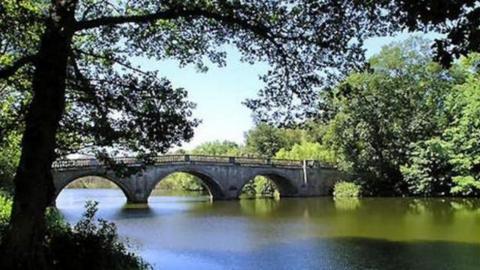 An ornate medieval stone bridge with a number of pillars and arches viewed from a riverbank 