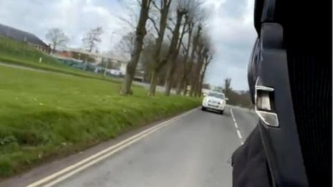 A motorcyclist filming himself driving away from a police car