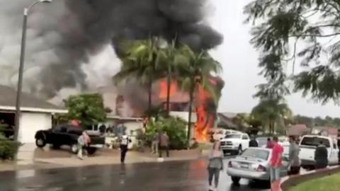 People look as smoke billows after a plane crashed into a house in a residential neighbourhood in Yorba Linda