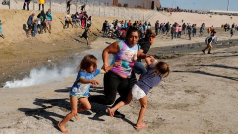 A migrant woman, Maria Meza, holds onto two of her daughters as she escapes the tear gas