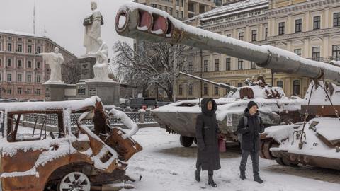 People walk in a snowy street with a tank turret in view, in Kyiv on 22 November