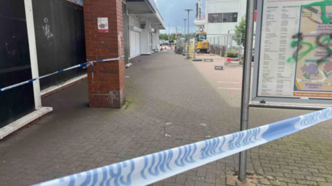 An empty paved street with blue and white police tape across it in the foreground 