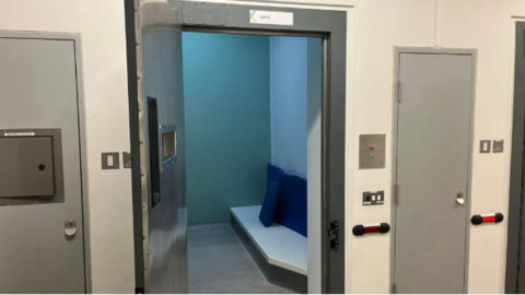 A custody cell with the door ajar, and other doors either side